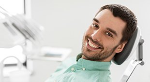 Man in light green shirt leaning back in dental chair and smiling