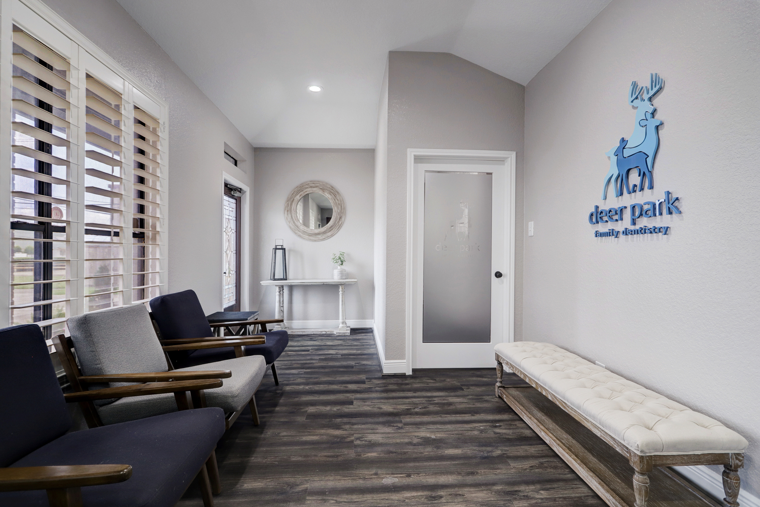 Cozy dental office reception area with seating – Deer Park Family Dentistry Reception area at Deer Park Family Dentistry featuring cushioned bench seating, modern chairs, hardwood floors, and the practice logo on the wall near the frosted glass door – Deer Park Family Dentistry